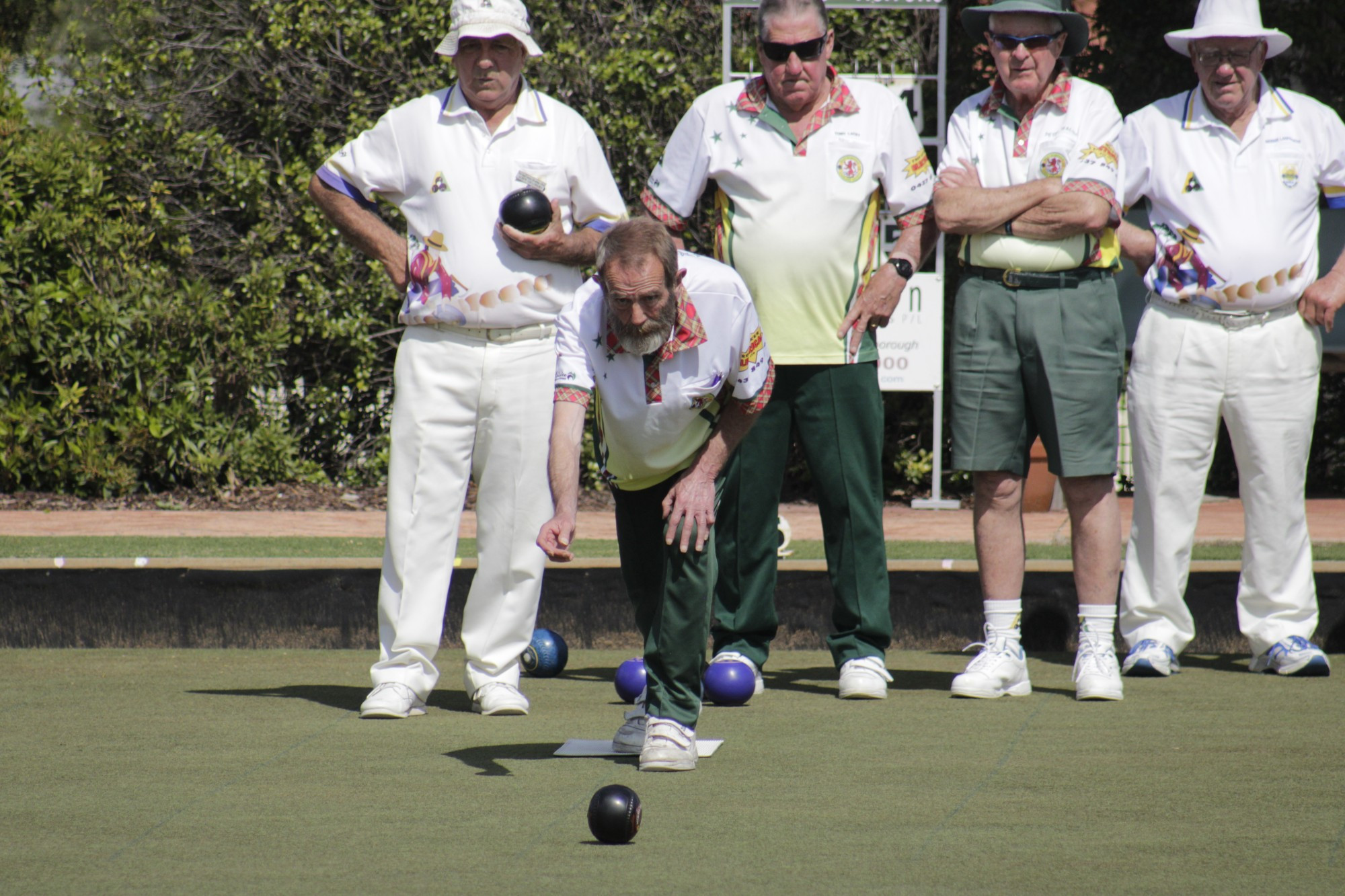 Alan Muggridge bowls for Highland Red with teammates and Dunolly Blue players watching intently.