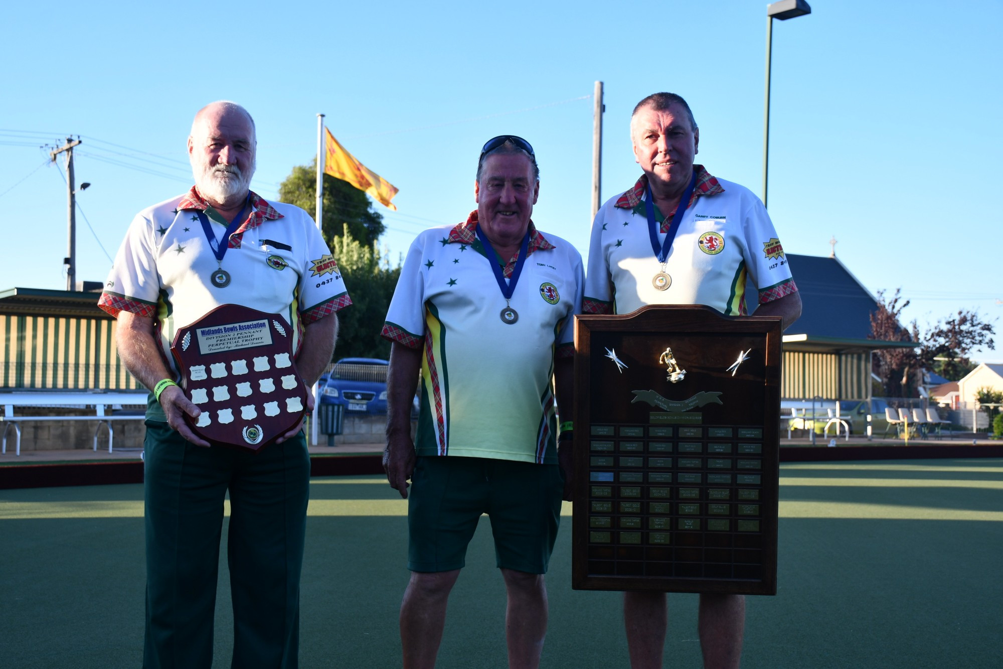 Side managers Bert Spencer (Highland Red, left) and Garry Coburn (Highland Tartan, right) flank Tony Lacey (middle) with Highland’s two premierships.